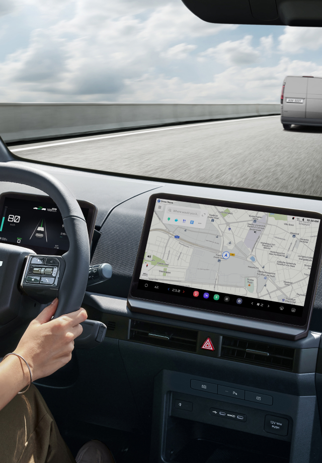 Innenansicht vom Fahrersitz mit Händen am Lenkrad und sichtbarem Navigationsbildschirm.